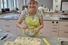 Frau steht mit einem Backpinsel hinter einer Küchentheke mit Teigrechtecken mit Obstfülle