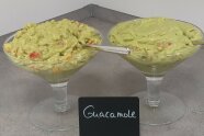 Zwei Glasschlaen mit grüner Avocadocreme und roten Tomatenwürfeln.