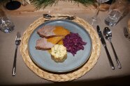 Auf einem in Naturtönen gedeckten Tisch steht ein Teller mit dem Hauptgang Sauerbraten mit Blaukraut und Semmelknödel in Form eines Gugelhupfs.