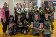 Eine Gruppe Frauen in Arbeitsschürzen zeigt Blumensträuße und -gestecke, die sie gefertigt haben.