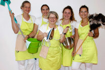 EIn Gruppenbild mit fünf Frauen in hellgrünen Schürzen und mit verschiedenen Geräten in der Hand.