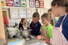 Kinder stehen an einer Küchenarbeitsplatte und beobachten wie ein Junge Mehl in eine Schüssel schüttet.