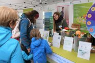 Kinder und Frauen stehen an einem Stand mit Infoftafeln und Lebensmitteln.